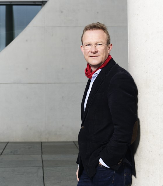 Maik Außendorf steht vor einer grauen Wand