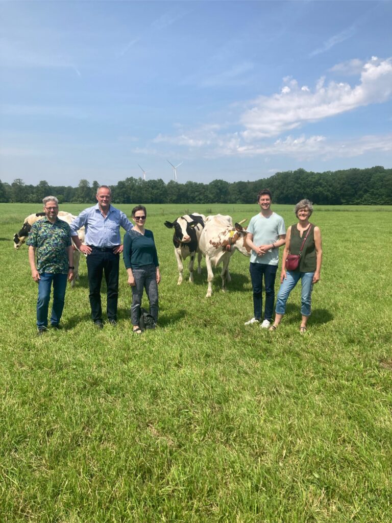 Fünf Menschen stehen in einer Reihe. Im Hintergrund sind Kühe und Windräder zu sehen.